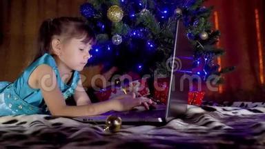 圣诞树下有笔记本电脑的女孩。 在新年里，孩子在一棵树下，手提电脑。 树下的一个小女孩
